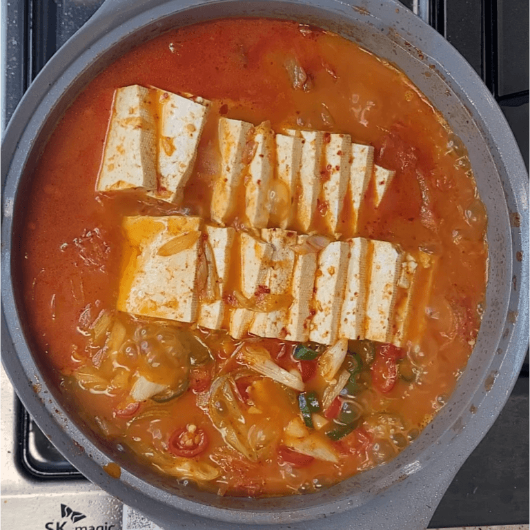 Kimchi jjigae bubbling in a pot with tofu and scallion