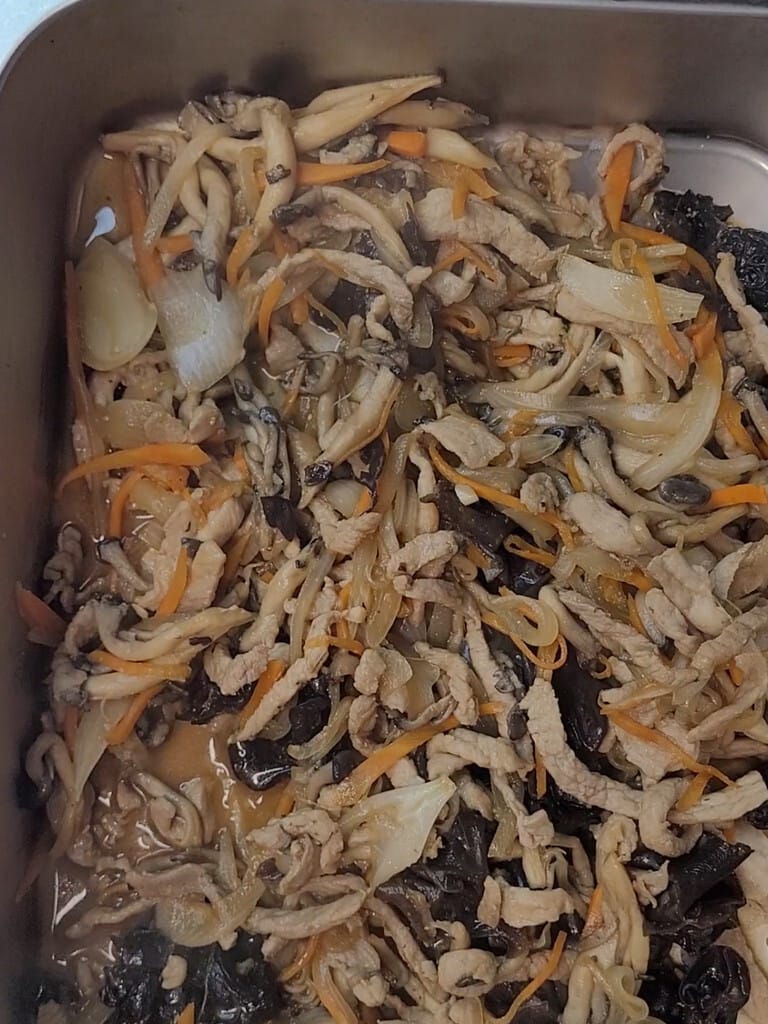 Cooked pork and vegetables set aside on a tray while the noodles fry
