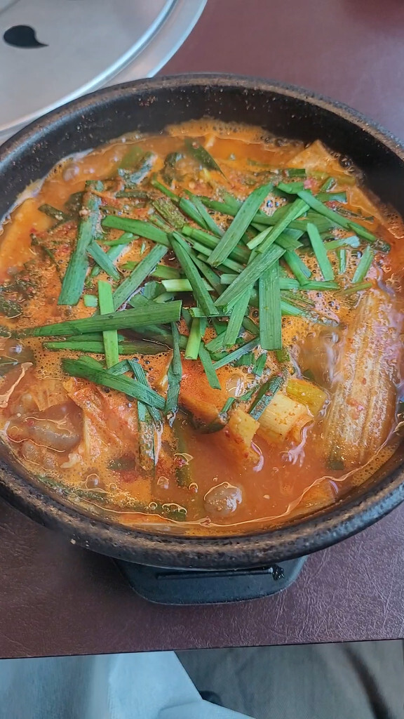 Red, spicy beef tripe soup topped with garlic chives in a one-person hot pot